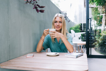 Carefree Caucasian woman with cup of hot caffeine beverage dreaming about leisure spending and...