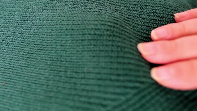 close-up of female hand touches knitted jersey, embossed canvas, green wool yarn, knitted texture, concept of warm things for cold weather, check quality, fashionable clothes, clothing production