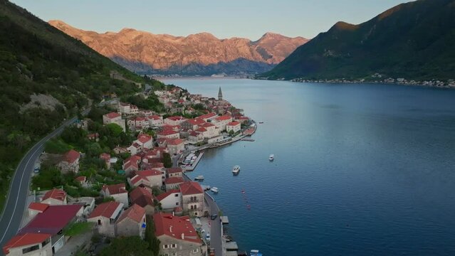 Famous balkan landmark - perast city in kotor bay of montenegro. aerial view at sunset, golden light of sun on the mountains in background. Fly over city roofs.