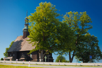 Bacówka w Piątkowej i okolice. Drewniany, mały kościół schowany za koronami zielonych drzew. 