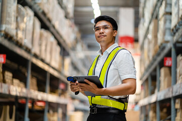 An Asian warehouse manager uses a tablet computer for checking goods in a warehouse. logistics and export business concept large warehouse.