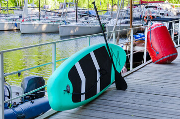 SUP board leaning against metal fence on pier. Subboarding board and paddle near the marina
