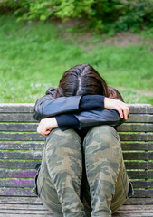 Young woman sad and depressed situated on park bench with arms and head on knees