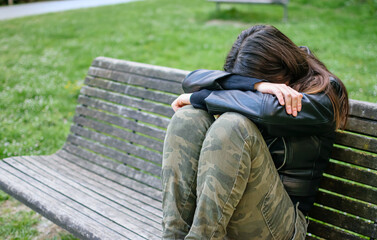 Young woman sad and depressed situated on park bench with arms and head on knees