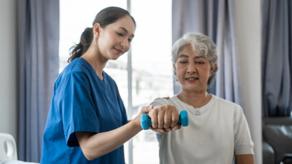 Obraz premium Young physiotherapist helping senior mature asian woman grey hair work out with dumbbells, to recover from injury at health centre in physical therapy session.