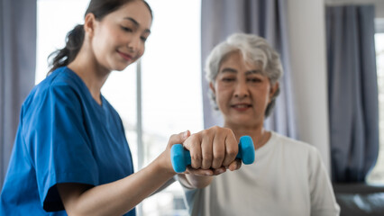 Young physiotherapist helping senior mature asian woman grey hair work out with dumbbells, to...