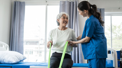 Young physical therapist caregiver assisting mature asian woman grey hair doing exercise with...
