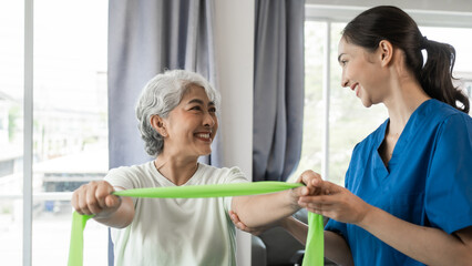 Young physical therapist caregiver assisting mature asian woman grey hair doing exercise with...