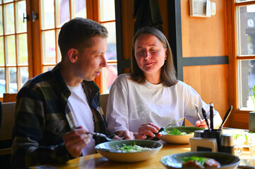 Sitting by a bright window in a cozy restaurant, a couple shares a meal together during lunchtime....