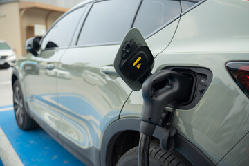 Selective focus of a power cable supply that plugged into a blurred green metallic car's charging port to charge pure electricity, that park on floor painted blue for recharging in charging station. 