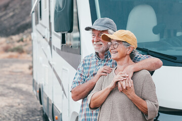 Happy senior couple on leisure trip enjoying travel destination standing outside a camper van...