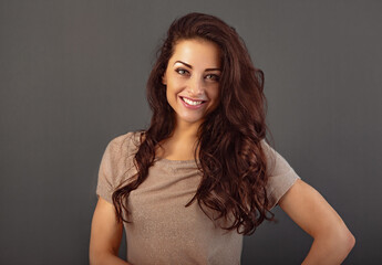Fototapeta premium Beautiful makeup toothy enjoying smiling woman with long brown healthy curly hair style in fashion shirt clothing. Closeup studio portrait on grey