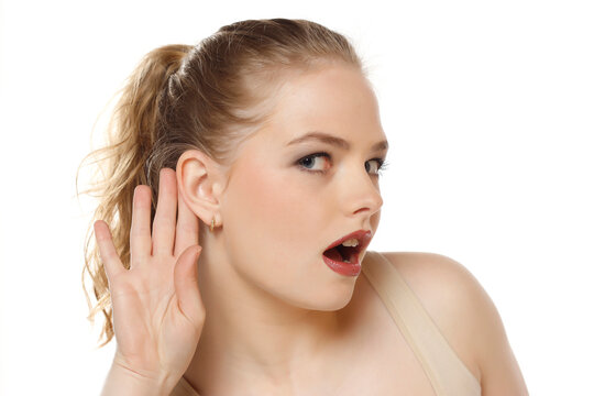 Young caucasian blonde woman listening to something by putting hand on the ear on a white background