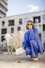Woman covers her nose from the stench of poop while cleaning up after her dog in the yard of an apartment building. Concept of cleaning up after pets in public place