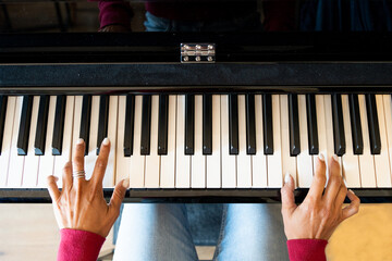 zenithal view of piano with woman's hands playing, white porcelain nails and fuchsia pink jumper