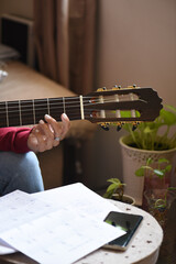 hand detail on the fret of a guitar, woman's fingers with white porcelain nails. girl on the sofa...