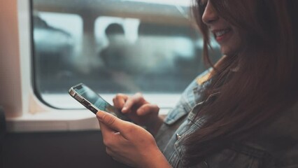 Close up - Smiling young tourist asian woman using mobile smartphone in a moving subway train, Female using social media on phone while traveling. - Powered by Adobe