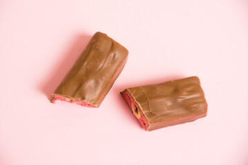 Pieces of appetizing chocolate bar with whole nut and strawberry on a pink background