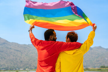 back of gay couple diverse friends standing and waving rainbow flags for celebrating equality sexual freedom, LGBT people enjoy outdoor activities at nature park during summer day in pride month