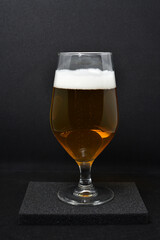 A glass of light beer on a black background. Fresh beer from a glass.