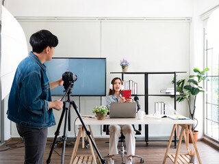 Asian pretty influencer woman review features technology gadget such as tablet, wireless headphone, microphone and notebook while photographer record live in studio room - obrazy, fototapety, plakaty