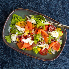 plate with salad with smoked salmon with mango and mozzarella on the table