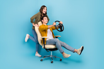 Full length photo of funny couple brother sister play push chair hold steering wheel fast speed driving excited isolated on blue color background