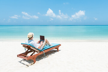 Young man working as digital nomad on the beach with a laptop