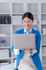 Sharing good business news. Attractive young businesswoman talking on the mobile phone and smiling while sitting at her working place in office and looking at laptop PC.