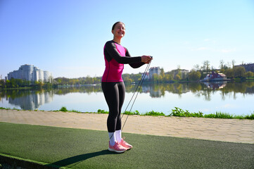 A young woman jumps on a skipping rope near the serene lake, with a focused expression on her face....