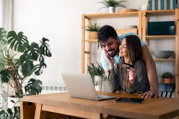 Young happy couple checking online bank account, making financial plans together, doing online shopping, booking a trip.