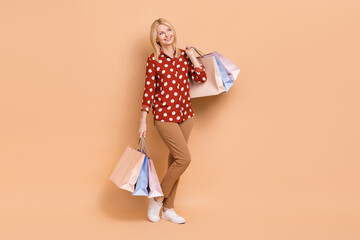 Full body photo of cheerful pretty lady hold store mall bags look empty space isolated on beige color background