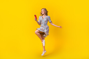 Full length photo of excited pretty lady wear flower print dress jumping high typing gadget isolated yellow color background