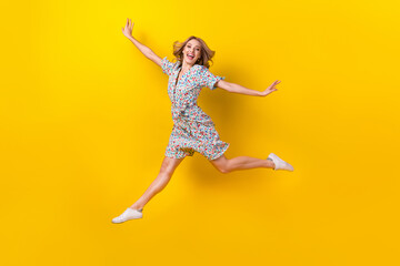 Full length photo of cute funky woman dressed flower print sarafan arms sides jumping high isolated yellow color background - obrazy, fototapety, plakaty