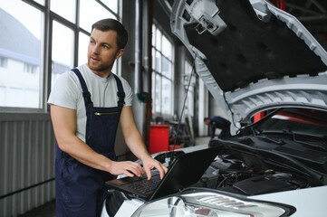 With laptop. Adult man in uniform works in the automobile salon.