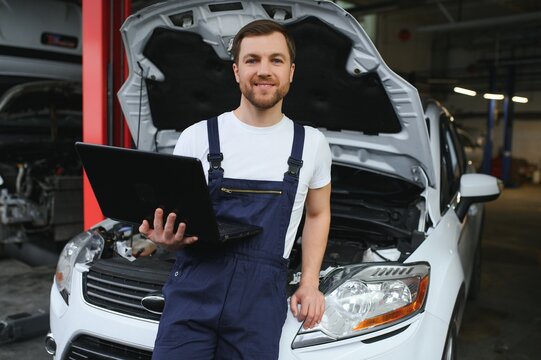 Mechanic man mechanic manager worker using a laptop computer checking car in workshop at auto car repair service center. Engineer young man looking at inspection vehicle details under car hood