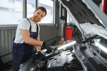 A mechanic is doing car checkup under the hood with flashlight at mechanic's shop.