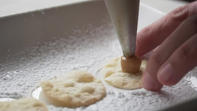 slow motion of pastry bag tip filling alfajor sheet, close-up