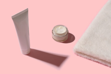 Cosmetic cream in a white tube and a white towel on a pink background.