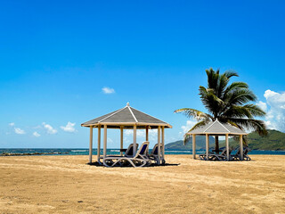 Relaxing Tropical vacation with beach cabana and palm tree under a blue sky.