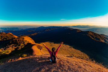 Confident girl sitting on the mountain. Big view landscape from Monjong. Tourist is relaxing in nature during sunset. Traveling sitting in Monjong, Chiangmai, Thailand. Rear view a woman is sitting.