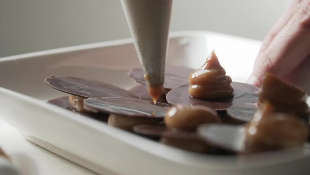 Close-up of the tip of the pastry bag filling alfajores with chocolate leaves, slow motion