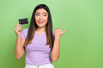 Photo of pretty japanese korean young girl hold credit card point empty space wear trendy purple outfit isolated on green color background