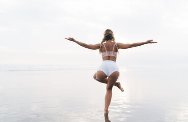 Back view of slim female yogi keeping healthy lifestyle and body wellbeing vitality, fit girl practice asana poses during sportive stretching at seashore beach - mindfulness enlightenment