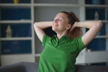 happy young woman sit on sofa and have a rest, relaxing living room at home in green polo t-shirt