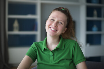 happy young woman sit on sofa and have a rest, relaxing living room at home in green polo t-shirt