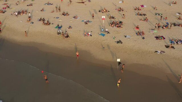 Aerial shot of people at beach in city against sky on sunny day, drone flying forward towards harbor