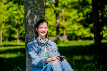 Young woman listening to the playlist of her smartphone sitting on the park grass