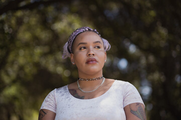 In a leafy forest, a nonbinary model of mixed African American and Latinx heritage poses confidently. Their purple braids shine, expressing their unique queer identity.
