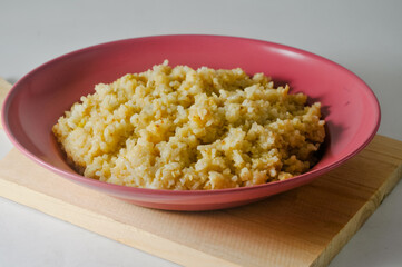Fried rice, an Indonesian specialty, is served on a red plastic plate on a wooden board isolated on a white background